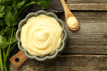 Delicious mayonnaise sauce in bowl and parsley on wooden table, top view. Space for text