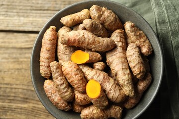 Tumeric rhizomes in bowl on wooden table, top view