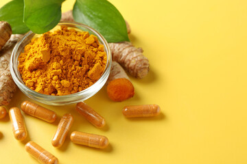 Turmeric capsules, powder, roots and green leaves on yellow background, closeup. Space for text