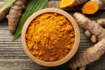 Turmeric powder in bowl, roots and leaves on wooden table, flat lay