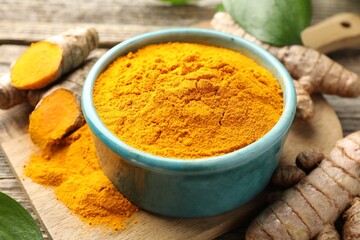 Turmeric powder in bowl and roots on table, closeup