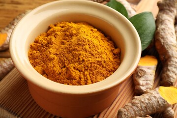 Turmeric powder in bowl, roots and leaves on table, closeup