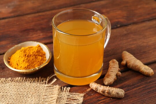 Aromatic turmeric tea in glass mug, roots and powder on wooden table, closeup