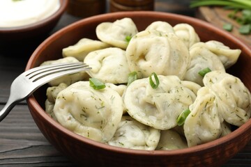 Tasty dumplings with green onion, dill and fork on wooden table, closeup