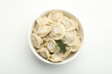 Tasty dumplings and dill in bowl on white table, top view