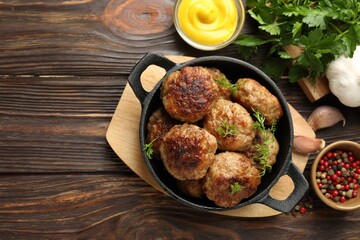 Tasty patties, dill in frying pan, mustard and peppercorns on wooden table, flat lay. Space for text