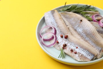 Marinated herring fillets with onion rings, rosemary and peppercorns on yellow background, closeup....