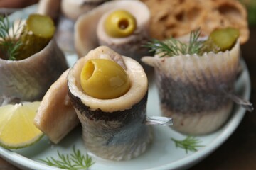 Delicious herring rolls with olives, pickles and dill on table, closeup