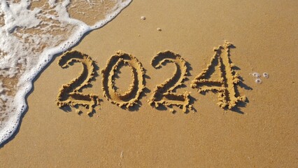 Fototapeta premium The year '2024' is written in the sand on a beach shore.