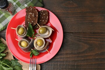 Delicious herring rolls with olives, parsley and bread on wooden table, flat lay. Space for text