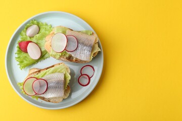 Tasty sandwiches with herring, radish and lettuce on yellow background, top view. Space for text
