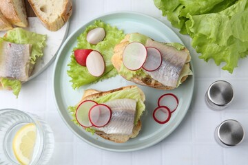 Tasty sandwiches with herring, radish and lettuce on white tiled table, flat lay