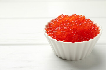 Tasty red caviar in bowl on white wooden table, closeup. Space for text