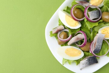 Delicious salad with herring, egg and vegetables on green background, top view. Space for text