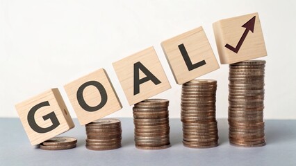 Coins stacked in ascending height with wooden cubes spelling ?GOAL?; financial objectives visualization