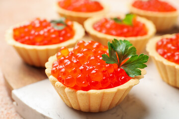 Tartlets with red caviar and parsley on beige table, closeup