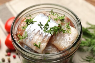 Pieces of delicious herring with dill in jar and tomatoes on table, closeup