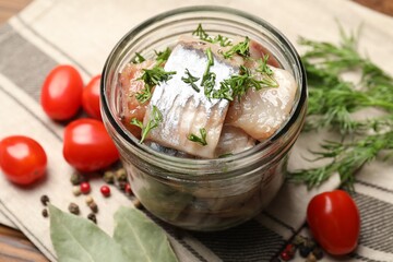 Pieces of delicious herring with dill in jar and tomatoes on table, closeup