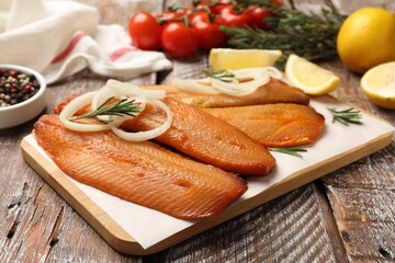 Delicious smoked herring fillets with lemon slices, onions and rosemary on wooden table, closeup