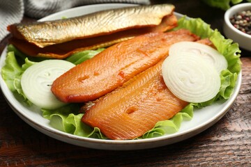 Delicious smoked herring fillets with onions and lettuce on wooden table, closeup