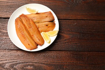 Delicious smoked herring fillets with lemon slices on wooden table, top view. Space for text