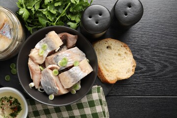 Pieces of delicious herring with green onions on black wooden table, flat lay