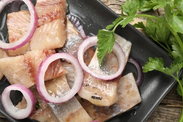 Pieces of herring with onions and parsley on wooden table, flat lay