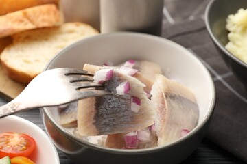 Eating delicious herring with onions at black table, closeup