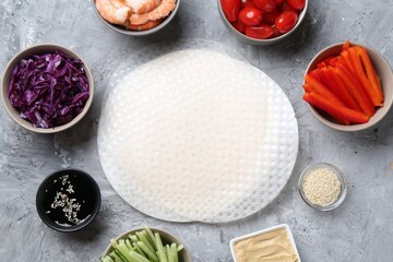 Rice paper sheets and different ingredients on light grey table, flat lay