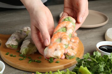Woman making tasty spring roll at grey wooden table, closeup