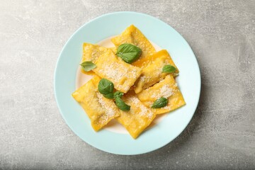 Delicious ravioli with cheese and basil on grey table, top view