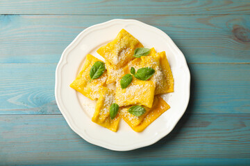 Delicious ravioli with cheese and basil on light blue wooden table, top view