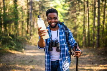 Young African American man smiling while taking a break with energy drink on a mountain trail.