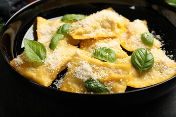 Delicious ravioli with parmesan cheese and basil on black table, closeup