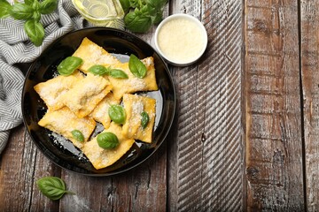 Delicious ravioli with parmesan cheese and basil on wooden table, flat lay. Space for text
