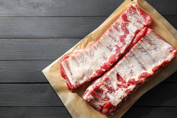 Raw pork ribs with sea salt on black wooden table, top view. Space for text
