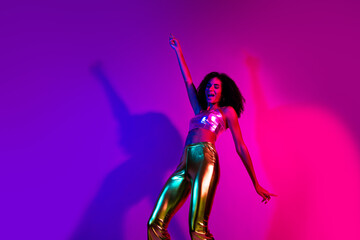 Young woman dancing joyfully under neon lights wearing trendy shiny outfit, radiating happiness and energy