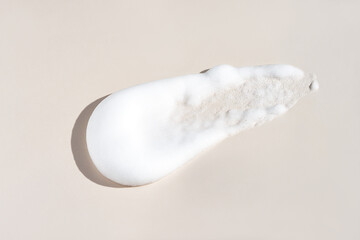 A close-up of a white foam or mousse skincare product on a neutral beige background.