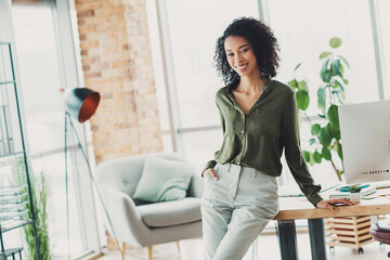 Confident young businesswoman in casual attire posing in a modern office workspace with bright natural lighting and stylish interior decor