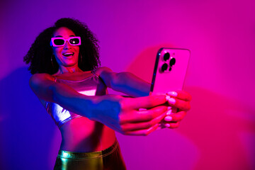 Stylish young woman in a neon-lit setting capturing a selfie with excitement and charm