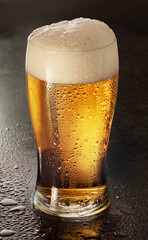 Glass of chilled light beer with beer foam head on black table top background.