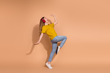 Young woman in casual outfit dancing joyfully with headphones on a pastel beige background