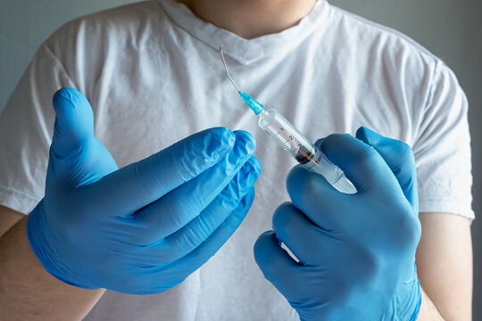 A doctor in blue medical gloves holding a syringe with a bent needle in front of themselves, close-up shot, a doctor or midwife holding a broken syringe.