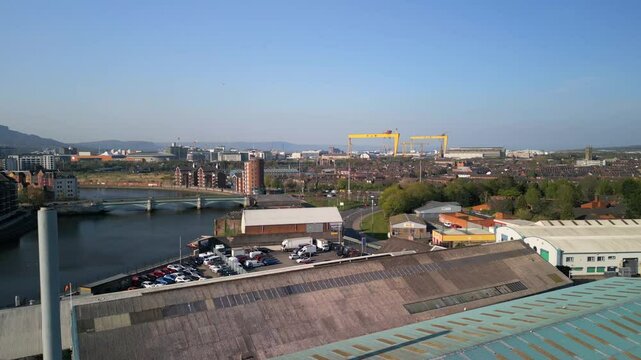 Aerial of Belfast City on a sunny summer day. Showing the Harland and Woolf cranes and the River Lagan, the camera moves forwards over industrial buildings. Filmed in 4K, 60fps and in Rec709 Color.