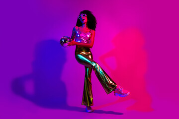 Fashionable young woman dancing in a neon-lit studio with a retro disco theme, showcasing vibrant style, confidence