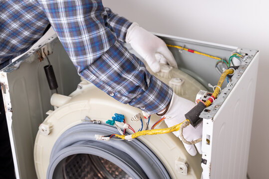 Repair service for washing machine with technician working on device internals. A technician repairs a washing machine, examining internal parts and wiring in a service environment - Powered by Adobe