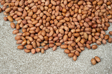 Pile of unpeeled brown raw peanuts on a gray background