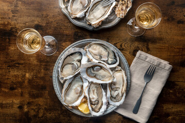 Fresh raw oysters on ice, overhead flat lay shot on a rustic wooden table, two platters with lemons and champagne