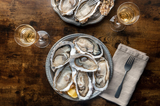 Fresh raw oysters on ice, overhead flat lay shot on a rustic wooden table, two platters with lemons and champagne