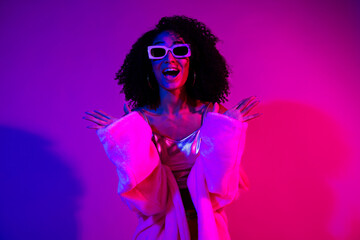 Stylish young woman in vibrant neon lighting with trendy attire, radiating joy and charm in a creative studio shoot